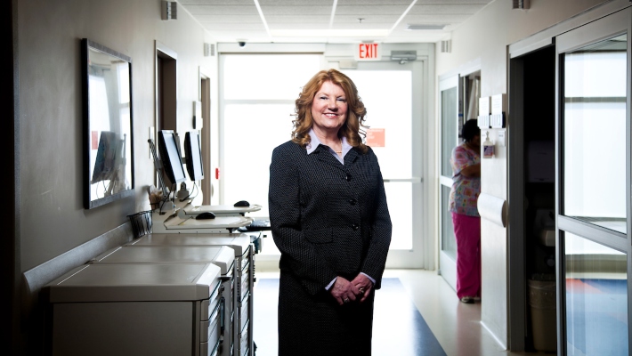 Nursing leader DNP 710x400 Nursing leader posing in hospital hallway wearing a suit jacket and skirt.