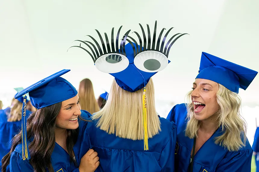 Two graduates look at the back of a decorated cap, which includes two large eyes and long, black eyelashes extending upwards