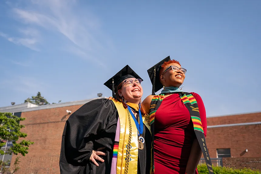 Two graduate students wearing stoles looking upward