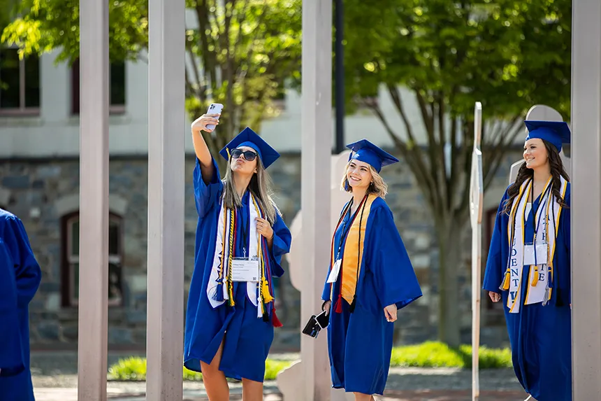 A grad in blue cap and gown takes a selfie of herself and another person