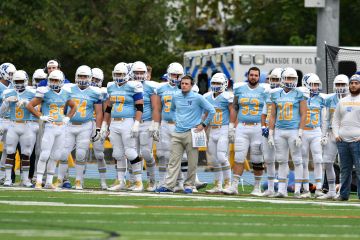 Coach stands on the field with several football players around him