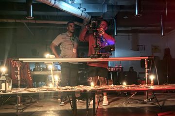 Two men work behind the scenes on a film production, with one holding a camera