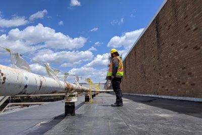 Student standing on roof of building in hard hat and vest