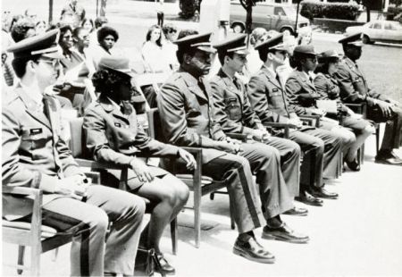 Black and white photo of men and women in Army dress uniforms seated in a row with others seated behind them.
