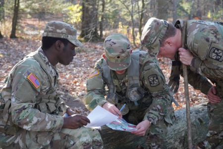 Three ROTC cadets in fatigues kneel over a paper in the woods during field training