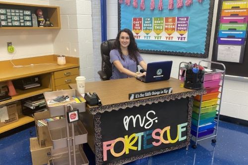Teacher sits at desk in elementary school classroom