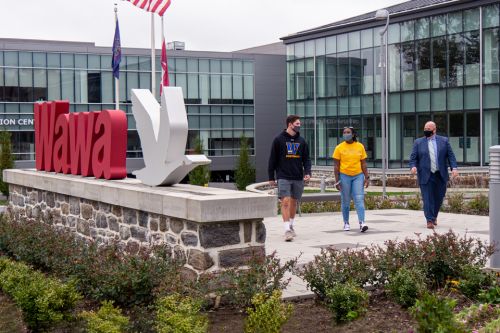Two students and an alumnus walk together past a Wawa sign at company headquarters