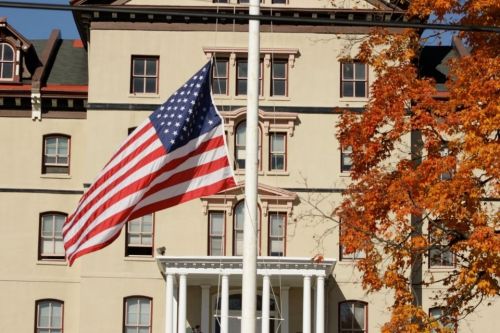 Flag on campus blowing in wind next to autumnal tree