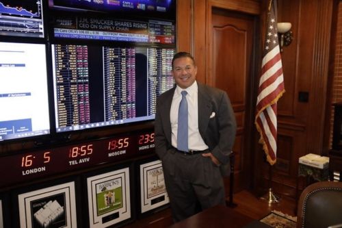 Ed Moldaver stands in his home office next to an American flag and stock market screen
