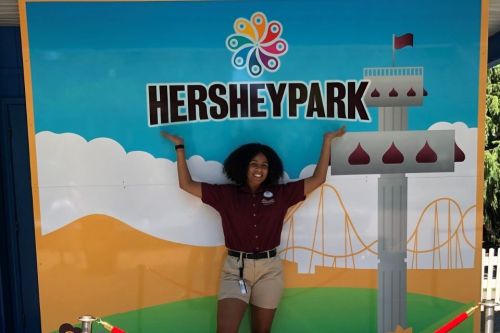 Student holds hands up above her head to point to a sign that says Hershey Park