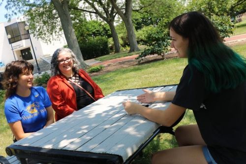Two students and a faculty member sit outside at a picnic table