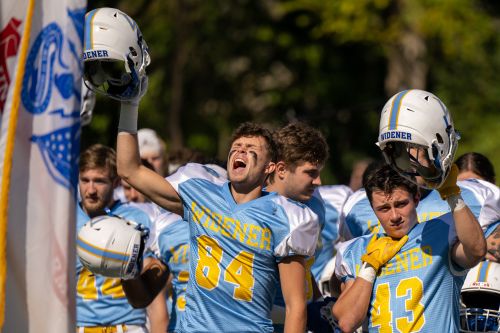 A football holds his helmet overhead and cheers for the team.