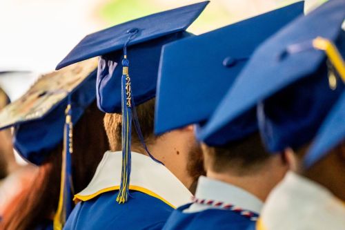 Graduates sit in a row at commencement. Their caps are visible with the 2024 tassel hanging down.