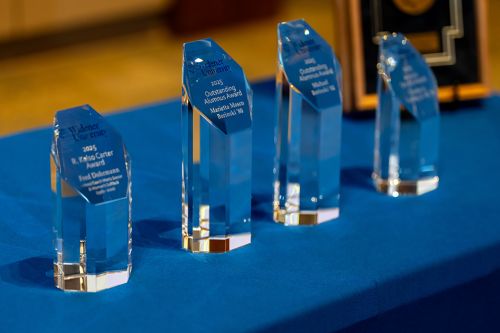 Five alumni awards sitting on a table with a blue tablecloth