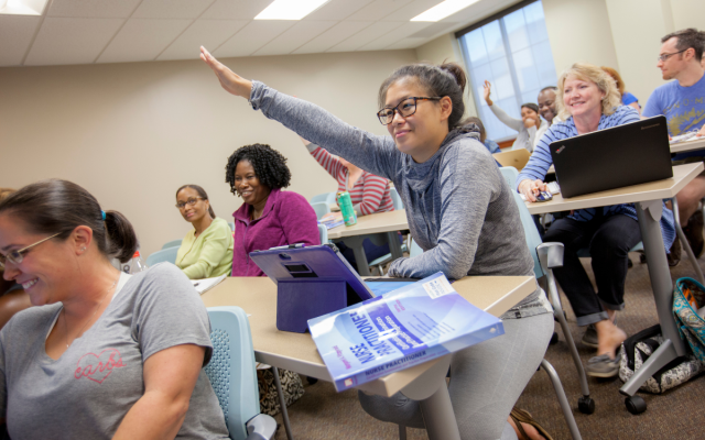 A graduate nursing student raises her hand in class.