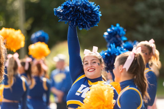 A Widener cheerleader smiles at the camera, waving her pom poms.